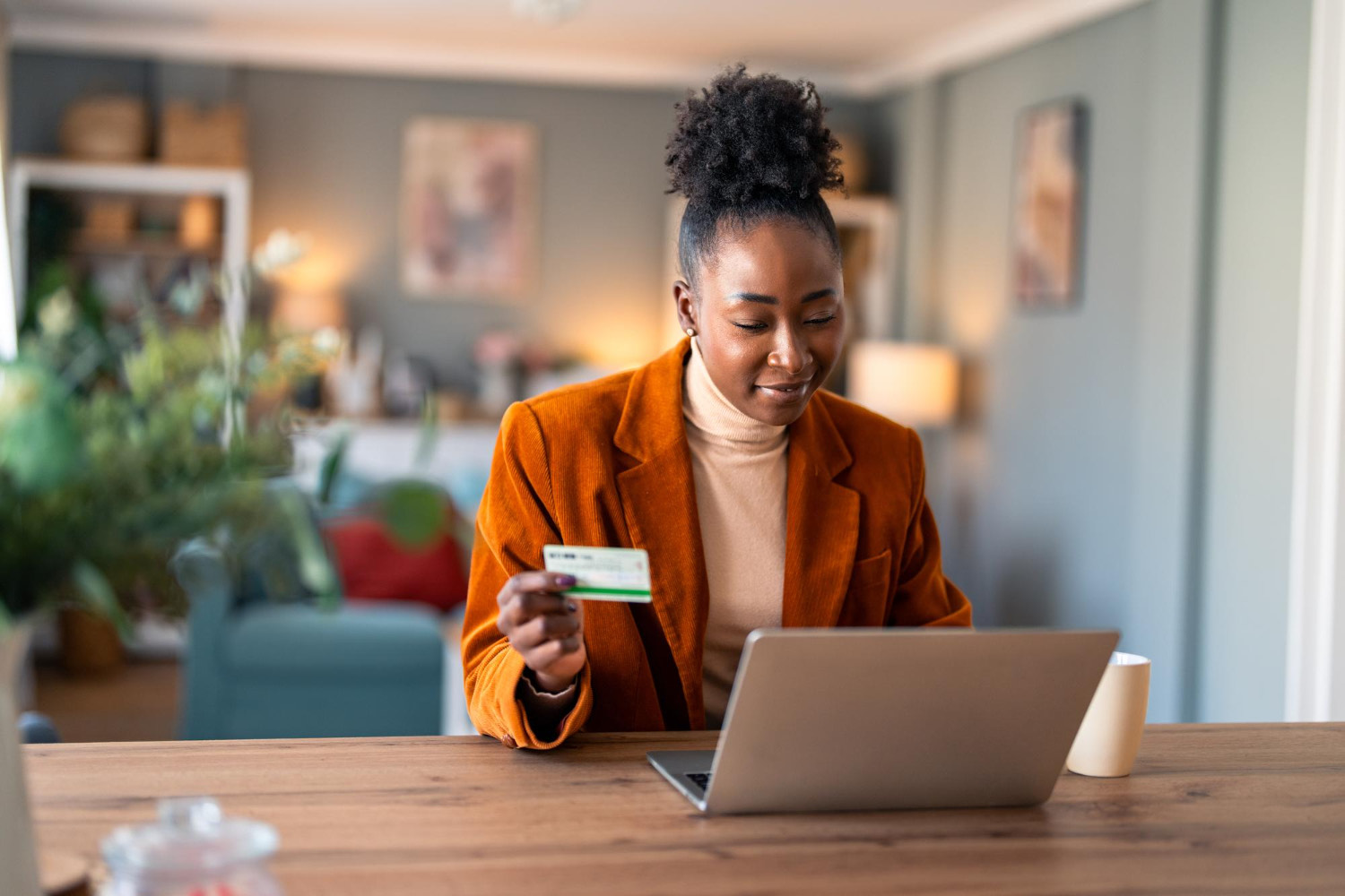 Woman shopping online on her laptop while holding a credit card at her desk.