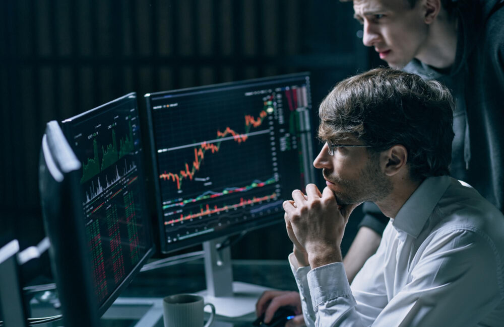 Two professionals reviewing financial data and transaction graphs on a laptop for Anti-Money Laundering (AML) compliance analysis.