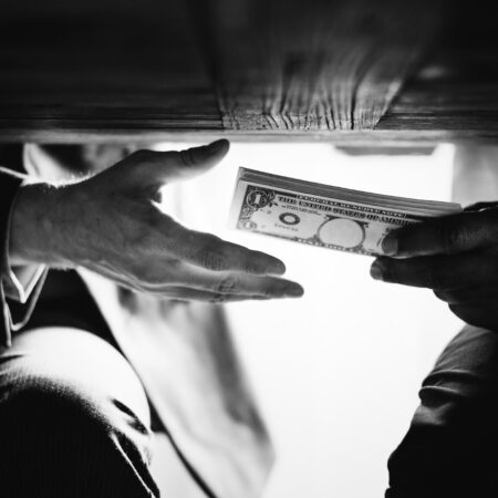 Hands exchanging cash under the table representing corruption, bribery, and financial crime risks linked to a politically exposed person (PEP)