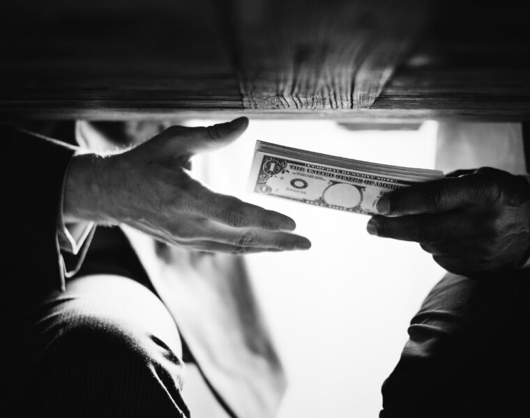 Hands exchanging cash under the table representing corruption, bribery, and financial crime risks linked to a politically exposed person (PEP)