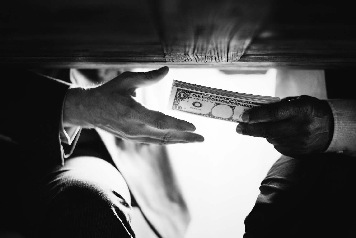 Hands exchanging cash under the table representing corruption, bribery, and financial crime risks linked to a politically exposed person (PEP)